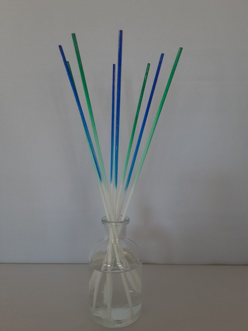 A glass vase with blue and green sticks in it.